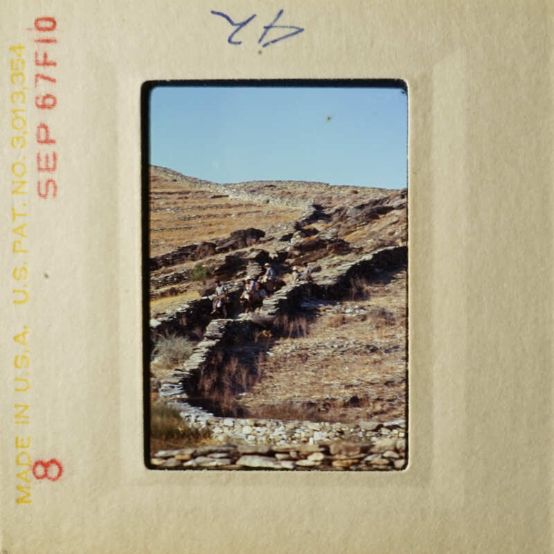 A photograph of an ancient stone wall with people walking along it, set against a clear sky and dry landscape.