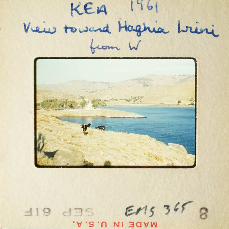 View from W towards Haghia Irini, 1961, with a body of water and mountains in the background.