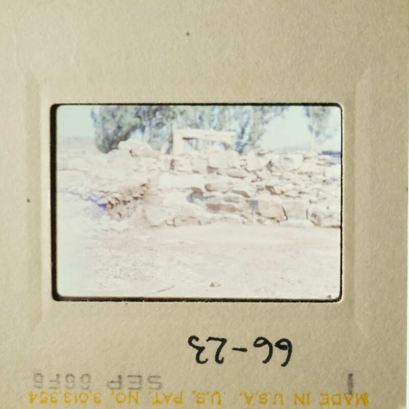 The photo shows an ancient stone structure, possibly ruins, with a barren landscape and a clear sky in the background.