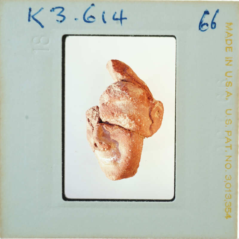 A photograph of a small, crudely made clay figurine resembling a human head with ears and facial features.