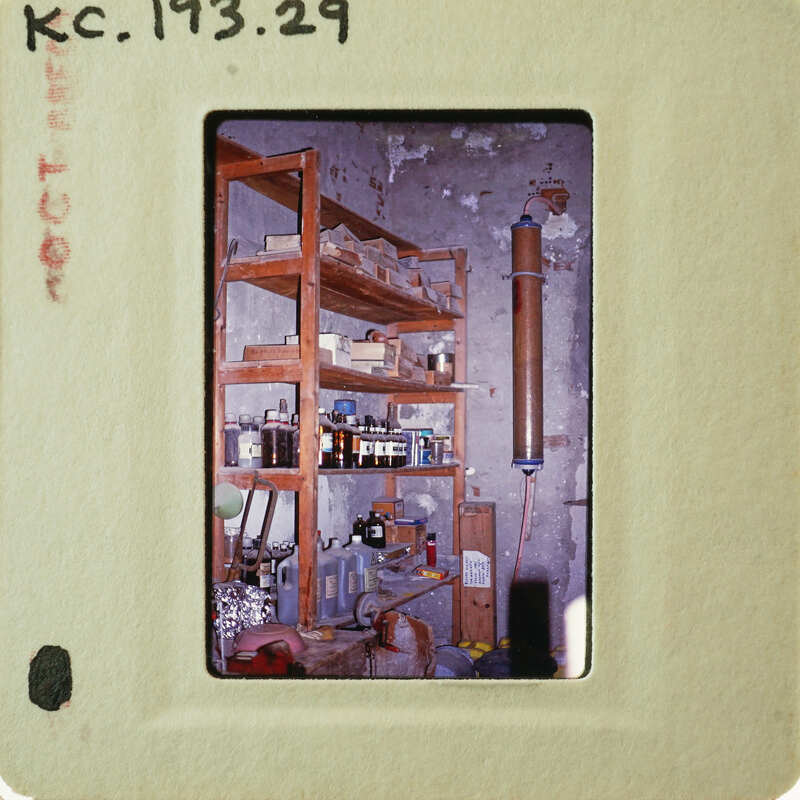 Old photo of a cluttered room with shelves and various items.