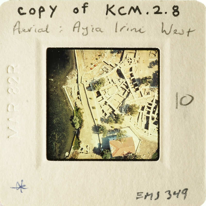 An aerial photograph of an ancient city, possibly Ayia Irini West, displayed on a small card with handwritten notes and numbers.