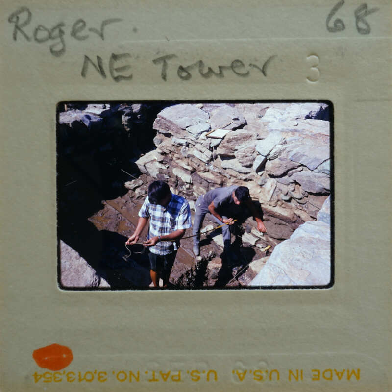 Two men working together on a rocky surface, possibly constructing or repairing a wall.