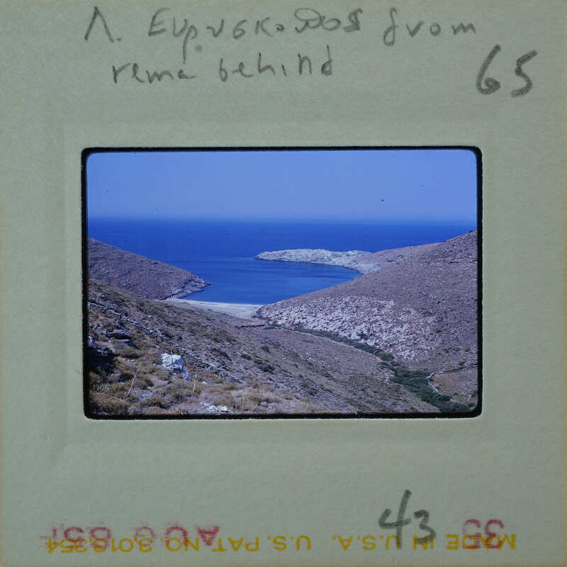 A vintage photograph of a coastal landscape with blue water and rocky hillsides, possibly from Greece.