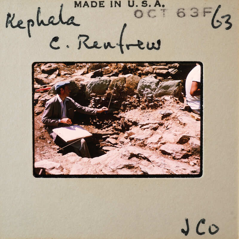 Man pointing at archaeological site with handwritten note on photo.