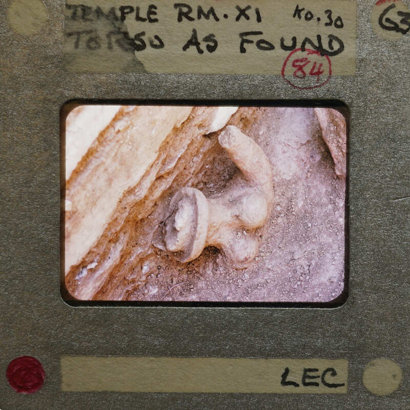 Torso of female terracotta figurine partially submerged in dirt.