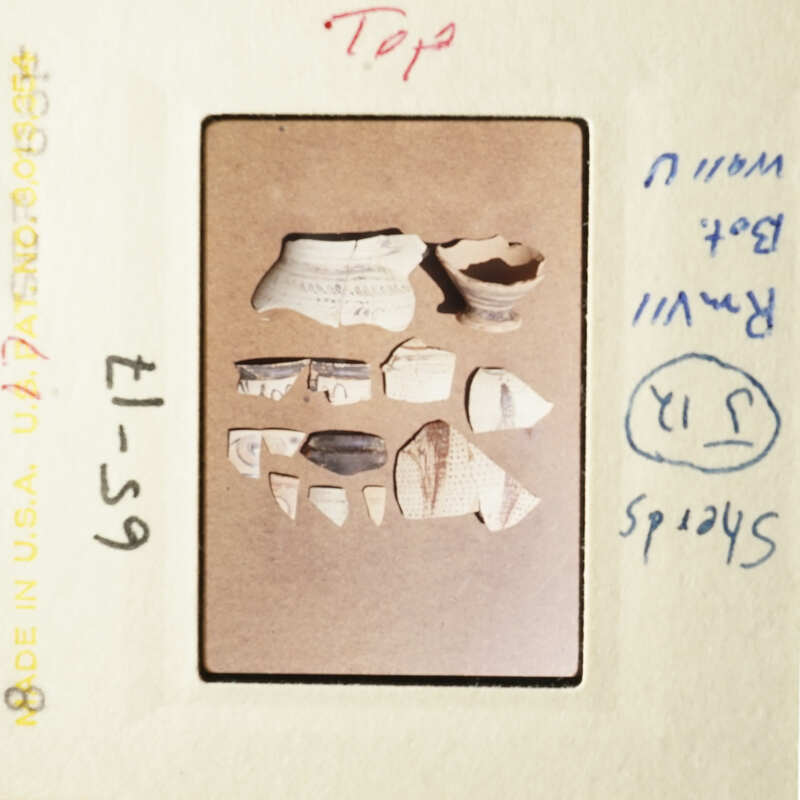 The image shows a collection of broken pottery pieces on a cardboard surface, with a handwritten note indicating they were found at the top of a hill.