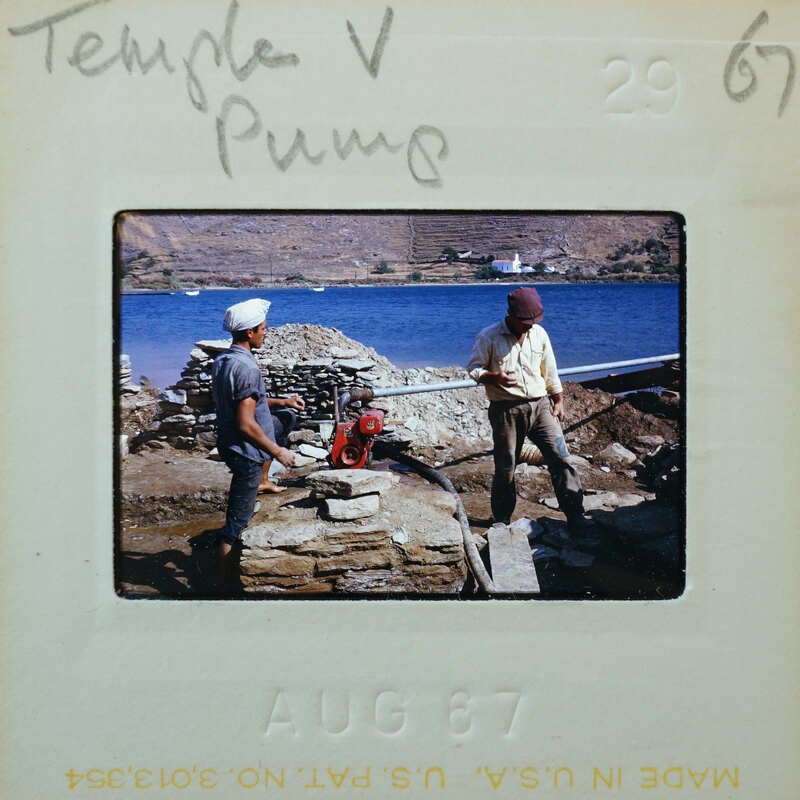 Two men working on a stone structure near water.