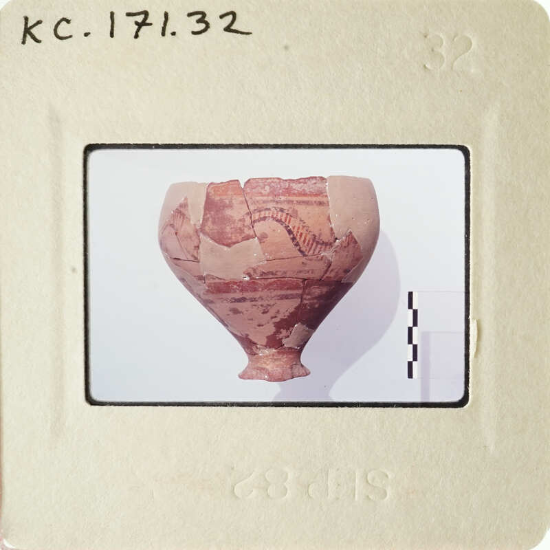 Ancient vase with intricate designs and missing pieces, photographed on a white surface.