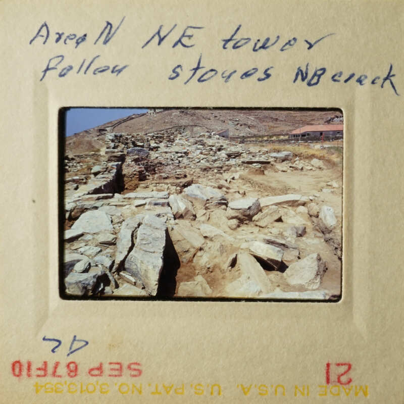 "A photograph of a rocky hillside with a sign indicating a tower and some writing."