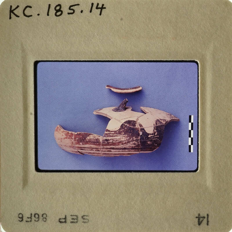 This is an image of a small, broken clay object with a handle and spout, possibly a cup or pottery fragment.