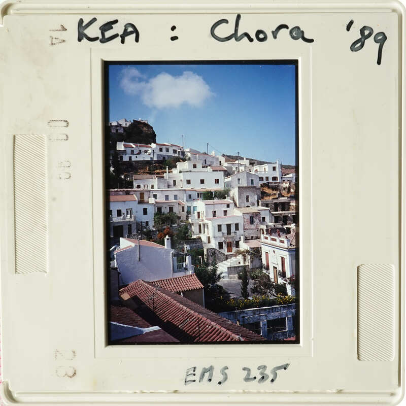 Old photograph of a village with white buildings and blue roofs, taken during the day.