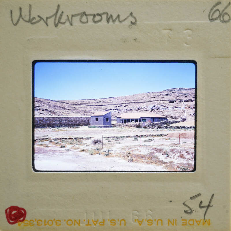 A vintage photograph of a desert landscape with a small building and sparse vegetation, enclosed within an old film strip frame.