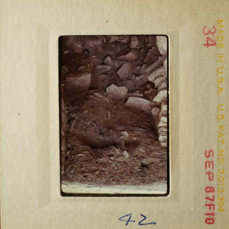 This is a photograph of an old slide depicting a rocky, earth-toned landscape with a small figure in the foreground.