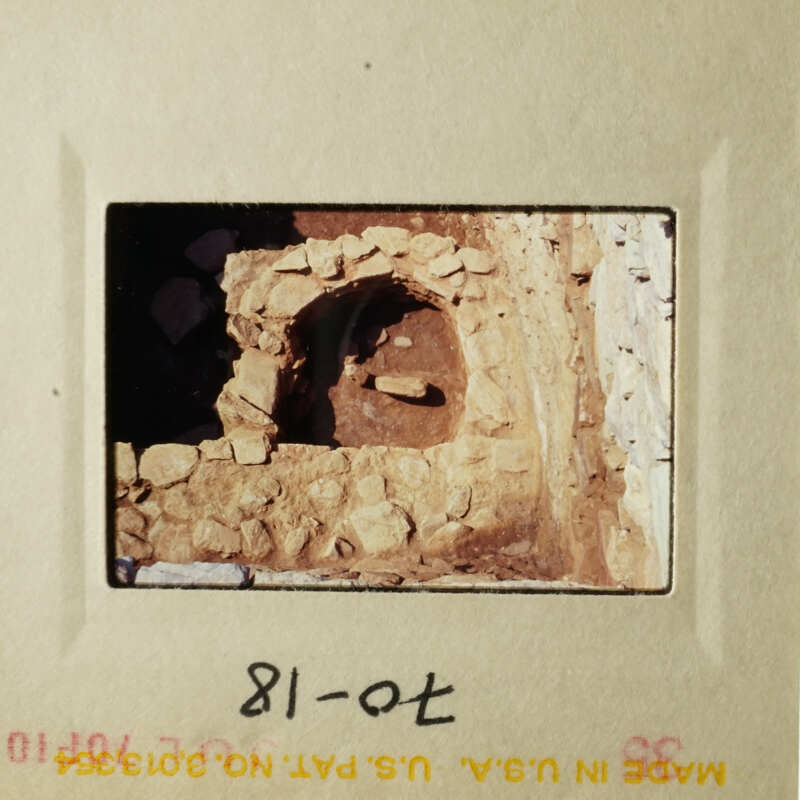 The photograph shows an ancient stone structure, possibly a cave with a small opening, set against a rock wall.