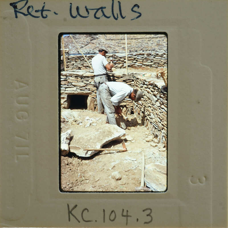 Two men working on a stone wall with tools.