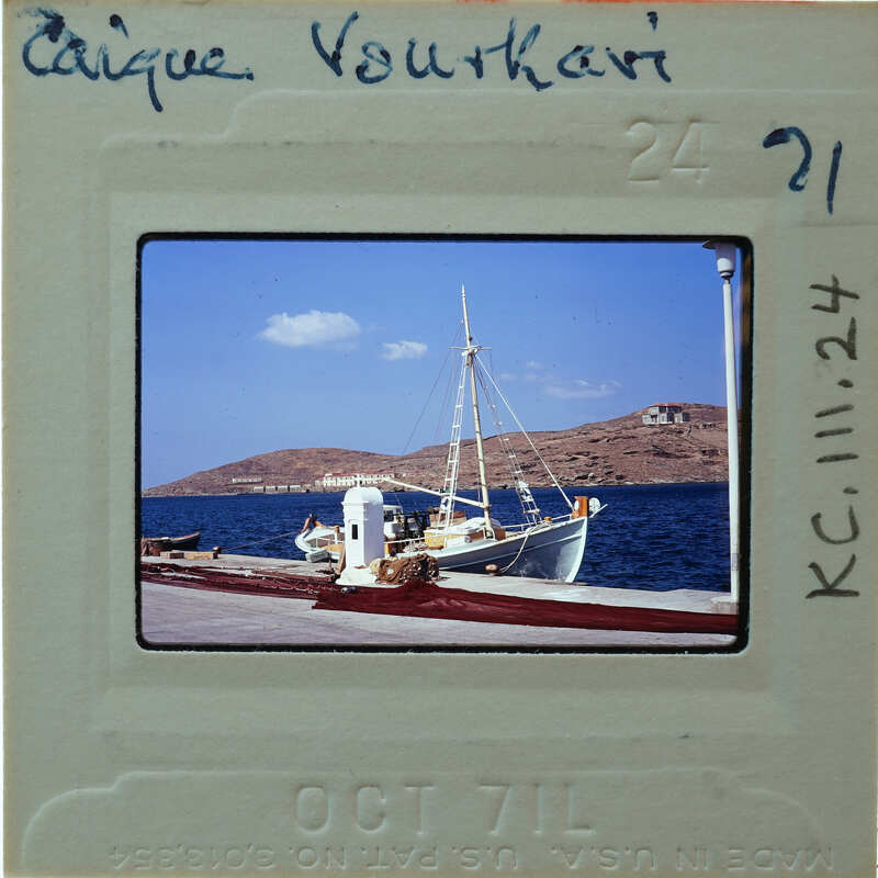 A vintage photograph of a boat docked at a pier with mountains in the background.