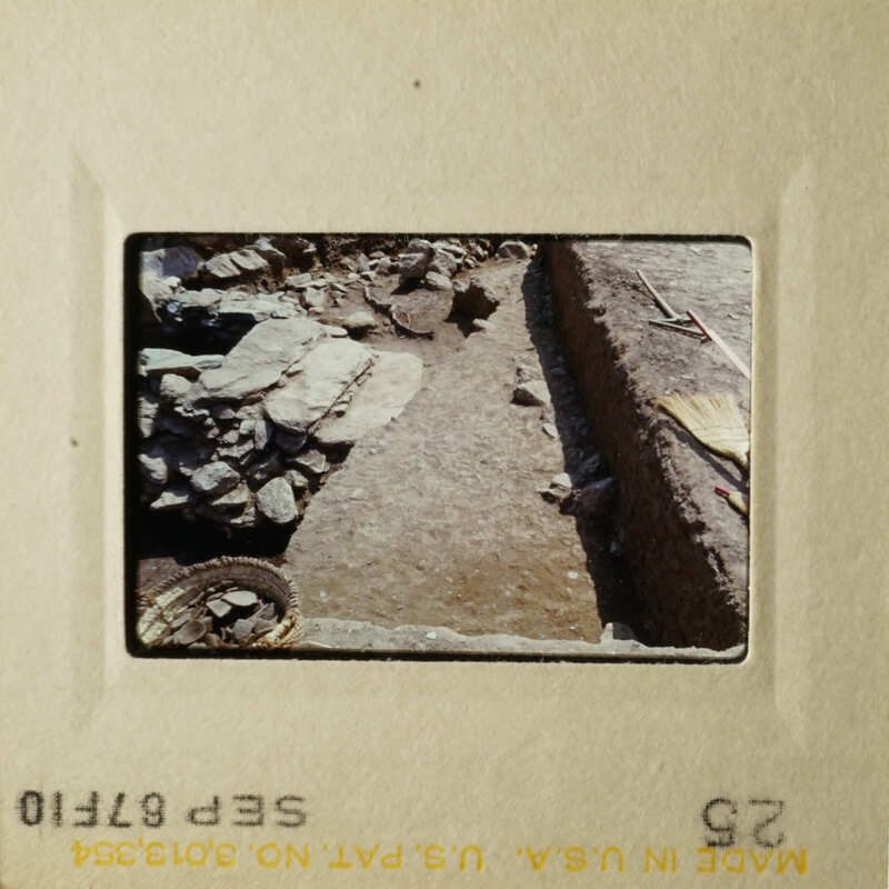 A photograph of an archaeological site with stone ruins, dirt path, and rocky terrain.