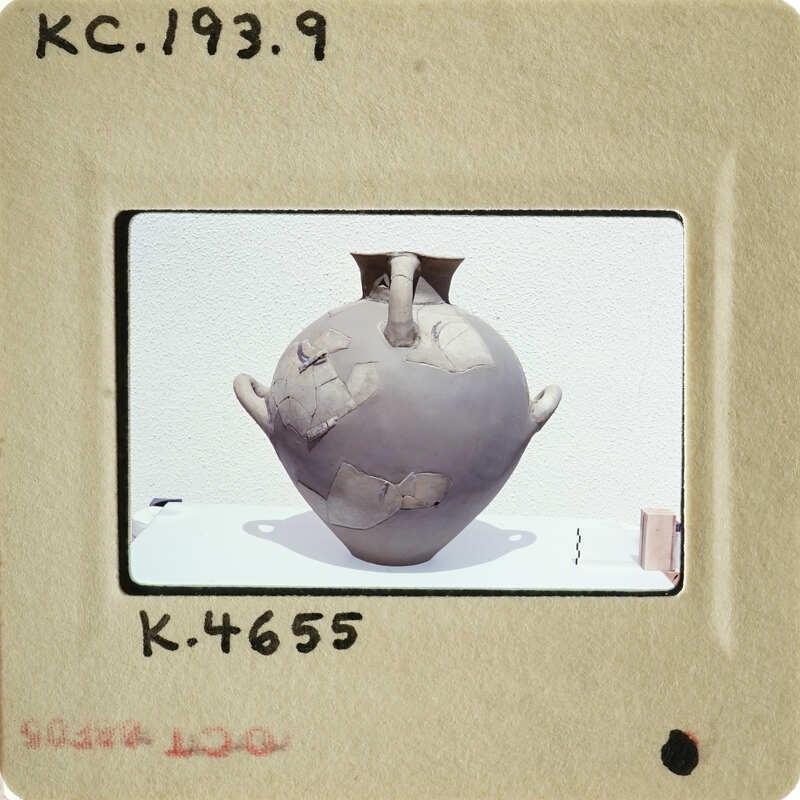 Ancient vase with visible cracks and wear, photographed on a white surface.