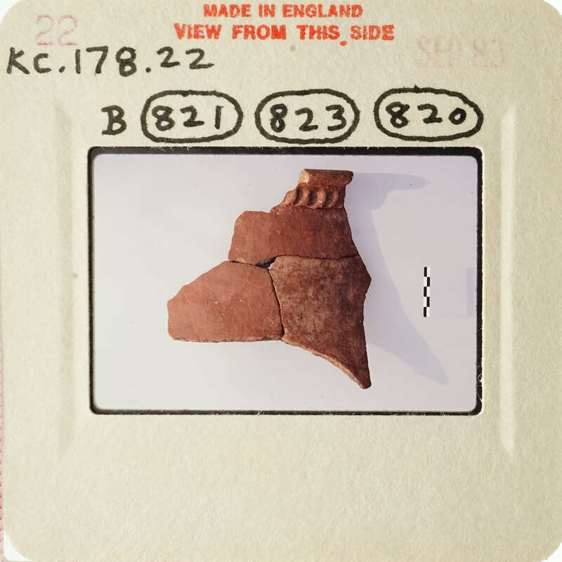 A photograph of an ancient clay artifact, possibly a pottery fragment, with visible markings and textures on display.