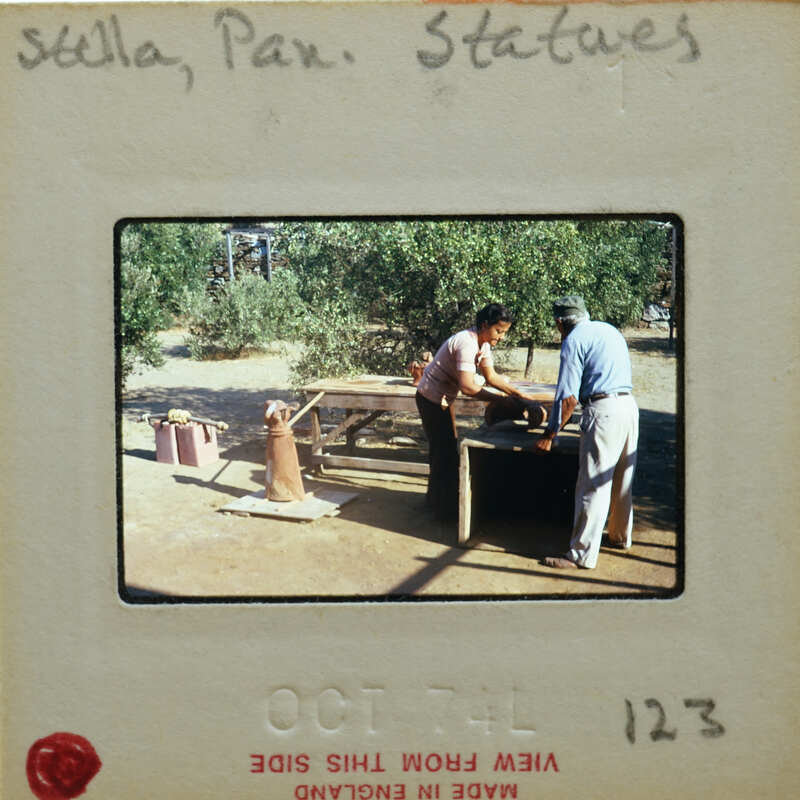 Two people repairing terracotta statues outdoors.