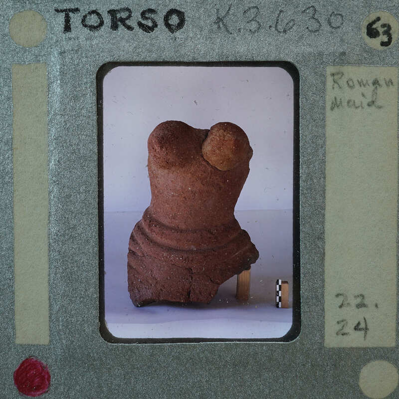 A small, damaged clay figurine on a white surface with a film strip border and annotations.