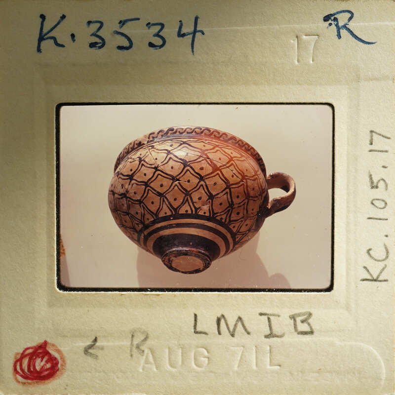 Photo of a clay pot with intricate designs, displayed on a paper with handwritten notes and dates.