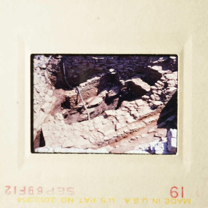 The photo shows an archaeological site with stone ruins and a dirt ground.
