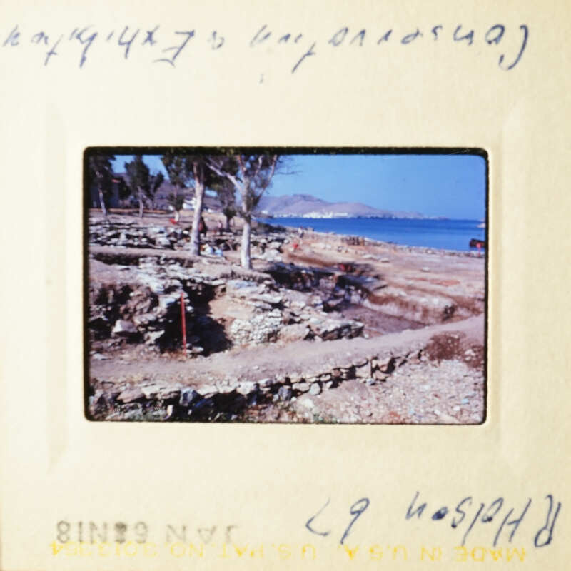 A photograph depicting an archeological site with ruins and a rocky beach, taken from a high angle perspective.
