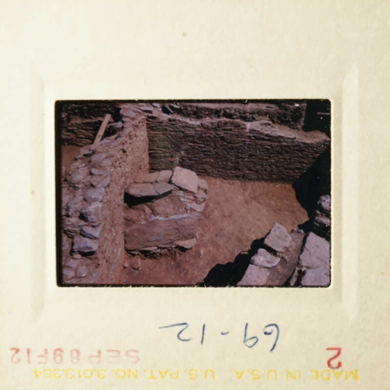 Ancient ruins in a dirt courtyard, with stone walls and debris, photographed from an elevated angle.