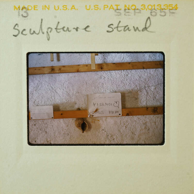 Photo of a sculpture stand with signs and labels, taken from an angle that shows the side of the structure.