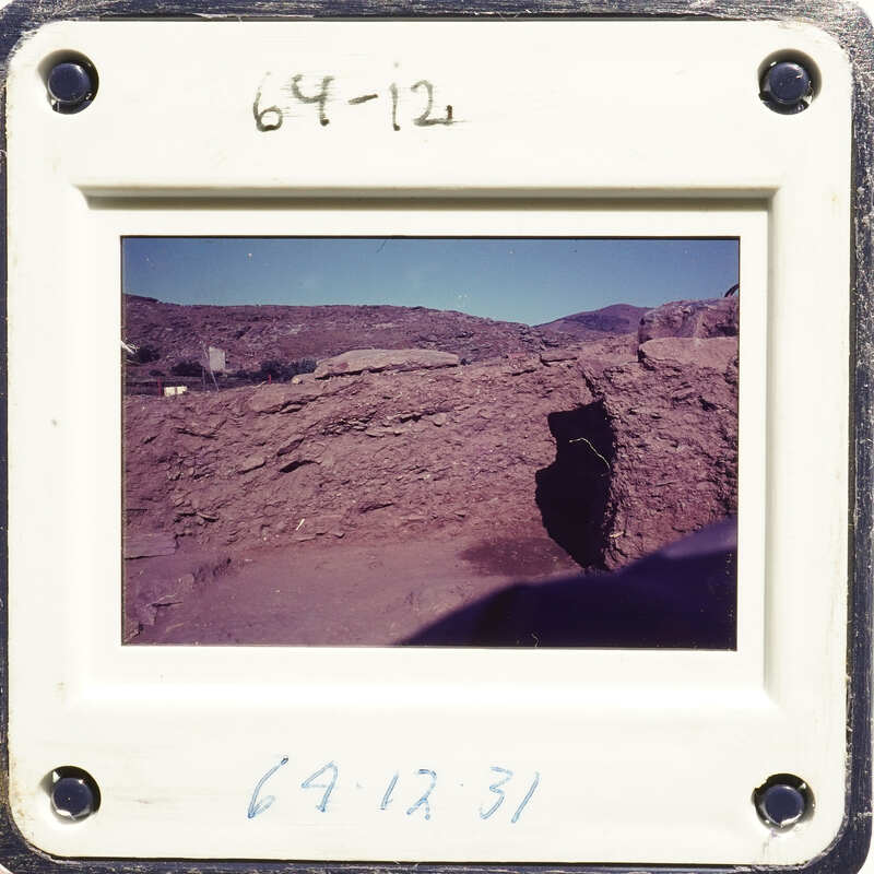 A photograph showing a rocky landscape under a blue sky with mountains in the distance.