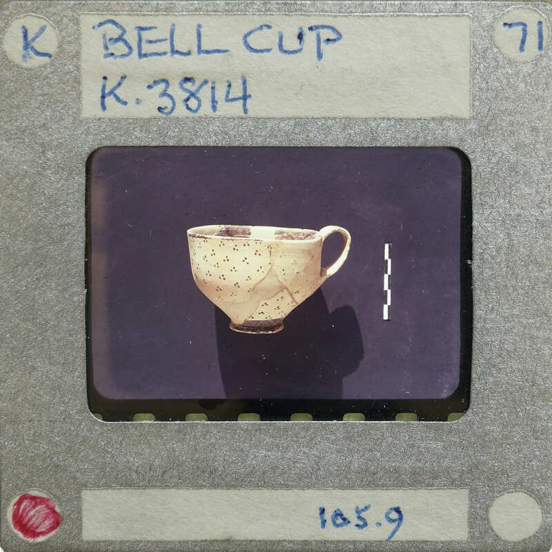 Broken cup (K.3814) in profile on black surface.
