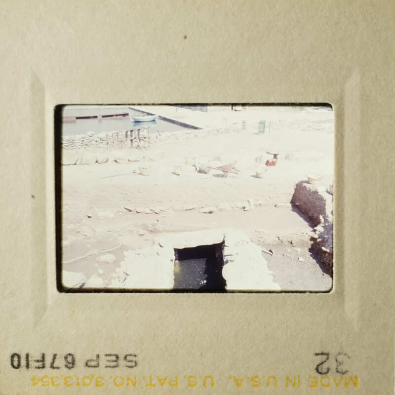 Archaeological trench with framed opening in floor and some rocks or rubble.