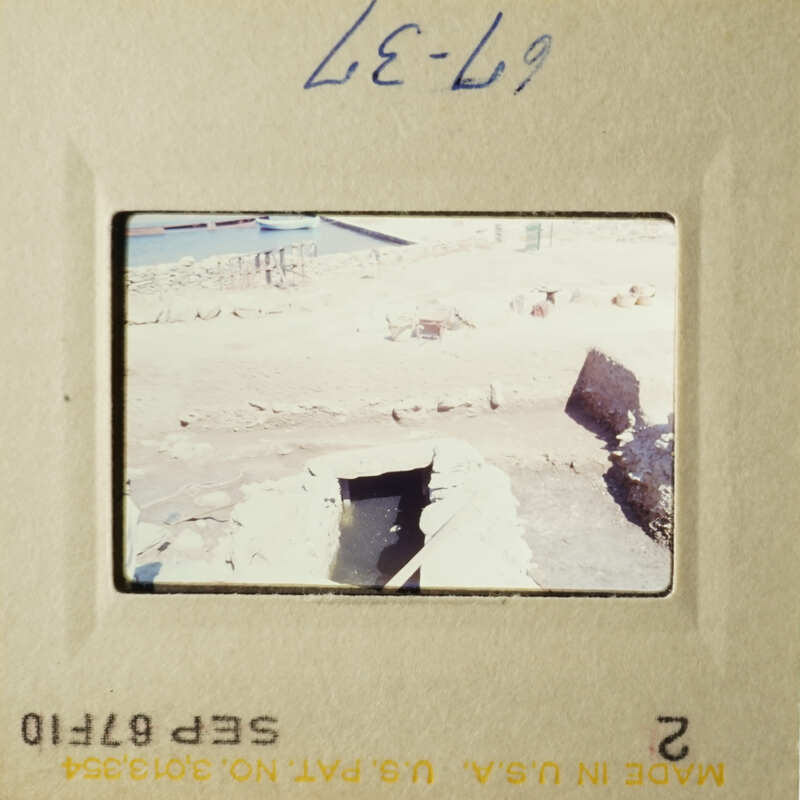 Archaeological trench with framed opening in floor and some rocks or rubble.