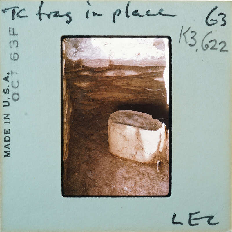 Broken base of terracotta figurine skirt on dirt floor surrounded by stone walls.