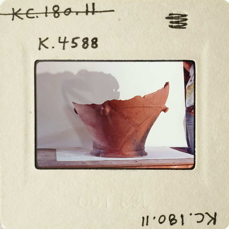 Old clay pot on display with visible damage and shadow cast on wall.