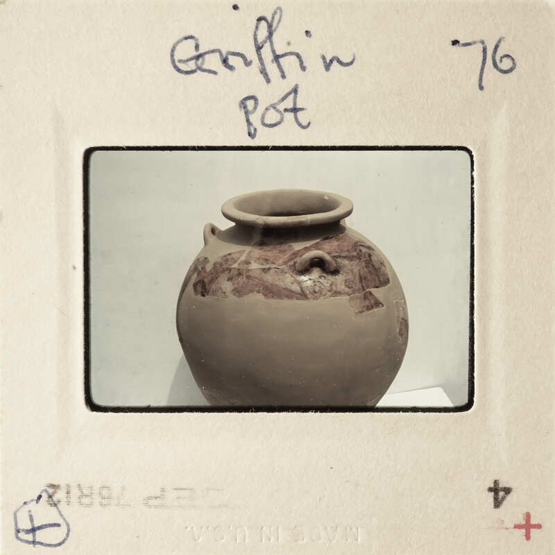 A brown clay pot with a handle and markings on it, photographed against a white background.