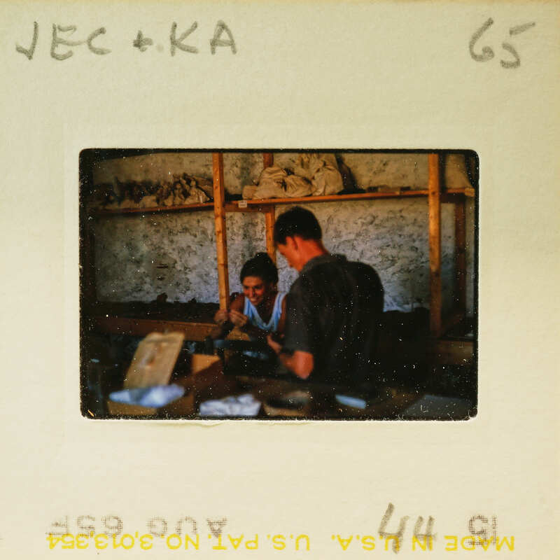 Two people working together on a project, possibly woodworking or crafting, with shelves and materials around them.