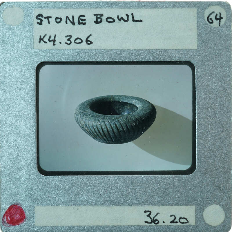 A photograph of a small stone bowl with diagonal incised lines from the side.