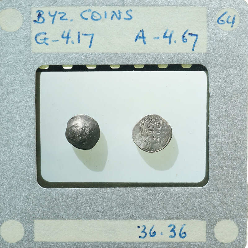 Two old coins displayed on a white stand with labels and numbers written on it.