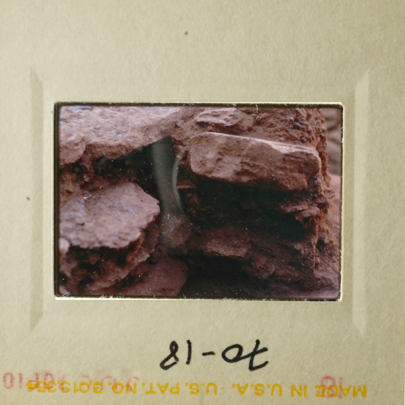 Photo of rock formation with red clay-like substance, possibly taken with an old camera.