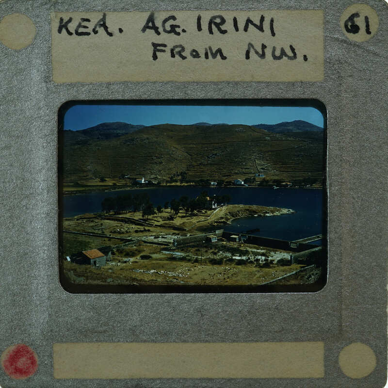 A vintage photograph of a coastal village with mountains in the background, displayed on an old film strip.