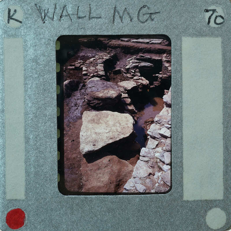 A photograph of a rocky wall, placed inside an old film strip container with handwritten notes on it.