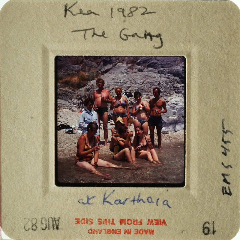 A group of people posing together on a beach, with some standing and others sitting in shallow water.