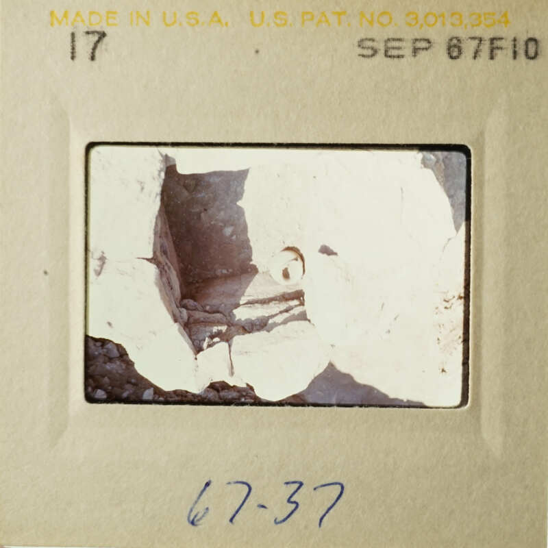 The image shows an old photograph with a black and white scene, possibly from an archaeological site, featuring broken stone structures.