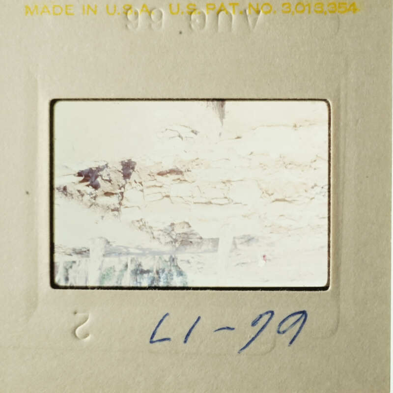 A photograph with a yellowed appearance, featuring a faded and blurry scene, possibly of a natural landscape or a building facade, with a blue handwritten note on the bottom left corner.