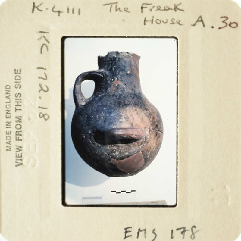 Ancient pottery with a face-like design, displayed on a white background.