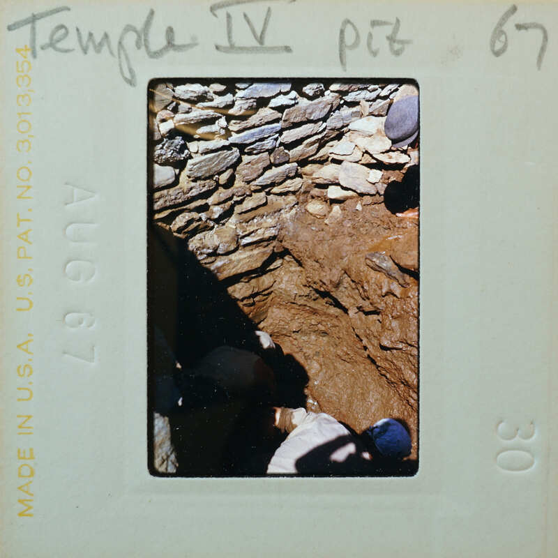 Stone wall with person excavating pit in front.