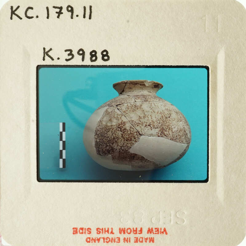 A photograph of an ancient artifact, possibly a vase, with visible damage and a measurement scale for reference.